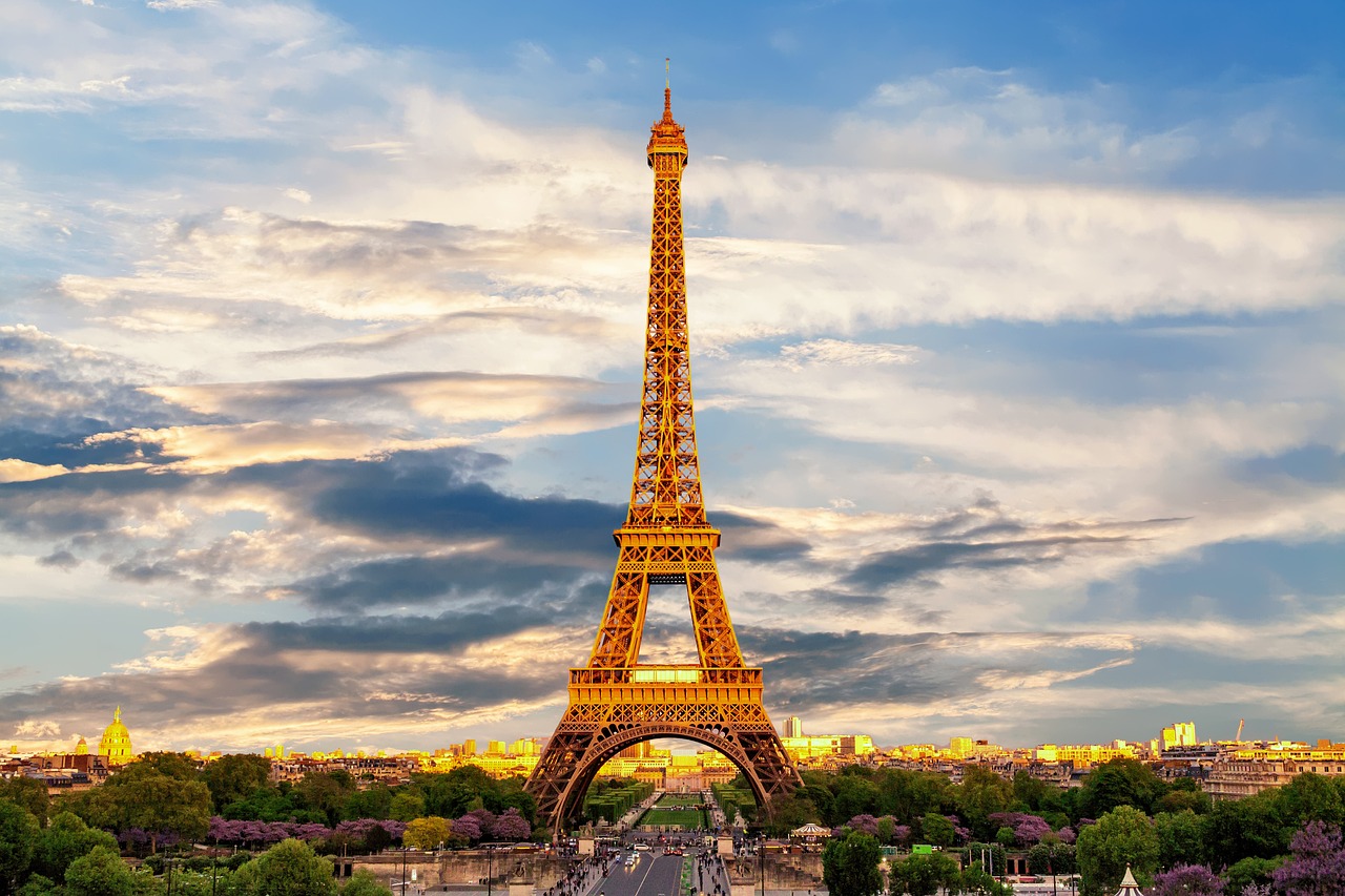 The Eiffel Tower in Paris, bathed in golden light, standing against a sky of soft blues and warm clouds—a symbol of memories, resilience, and returning to a place filled with both loss and survival.