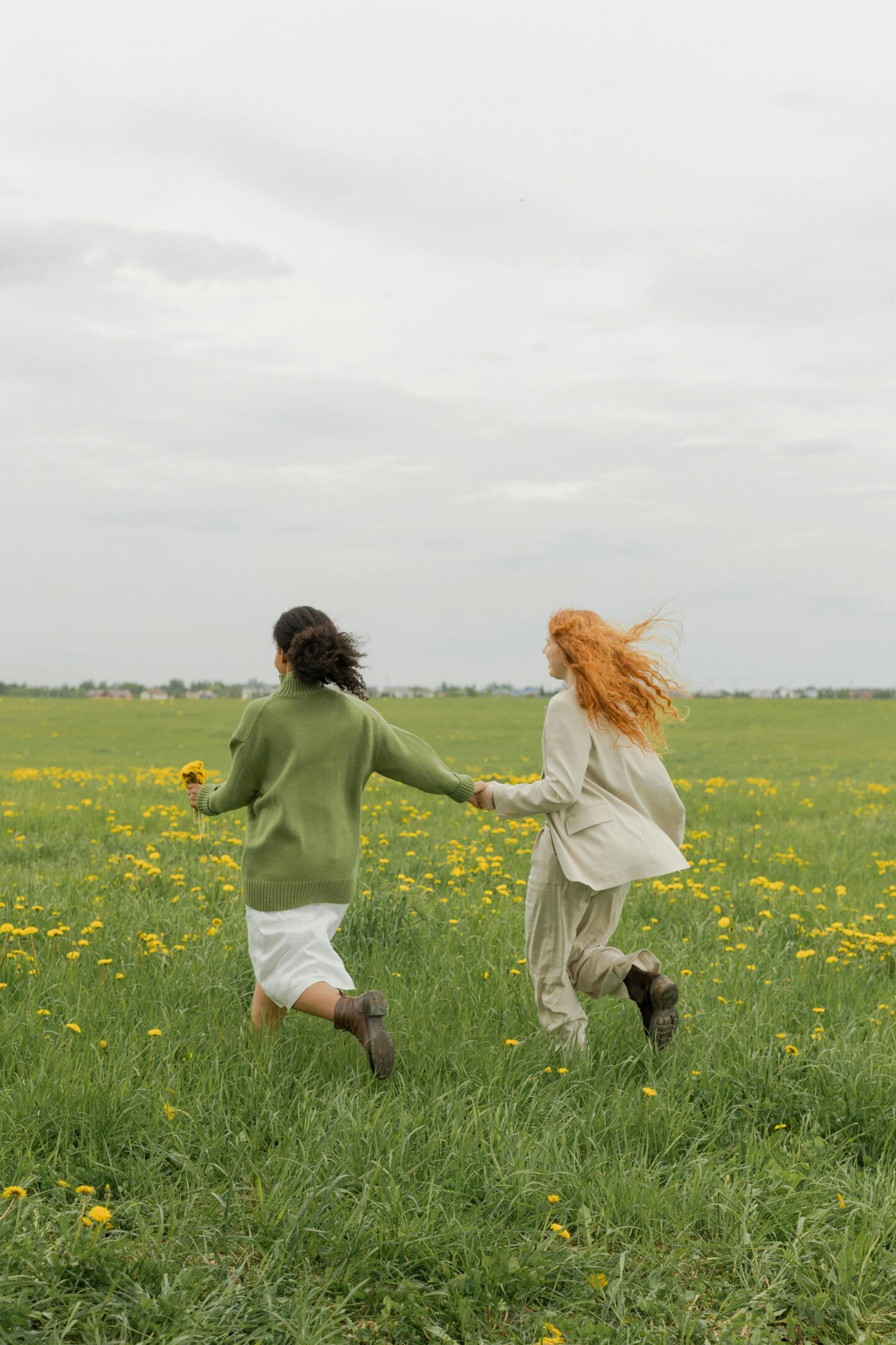 Two women holding hands and walking through a field of flowers, symbolizing emotional support and friendship—representing how to help your friend struggling with infertility.