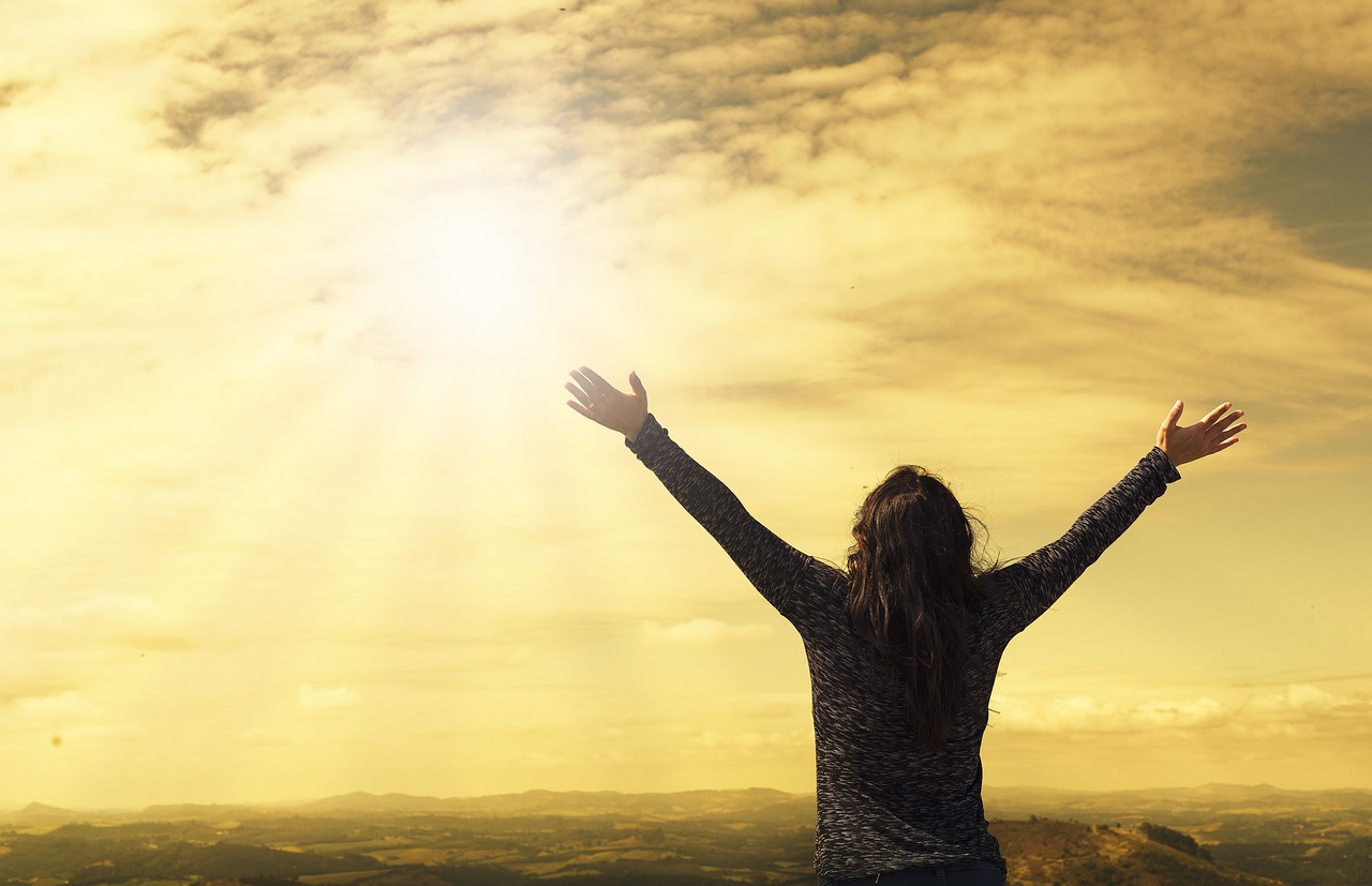 Woman standing on a mountaintop at sunrise with arms raised in strength and freedom, symbolizing empowerment and healing after infertility for those who are childfree not by choice.